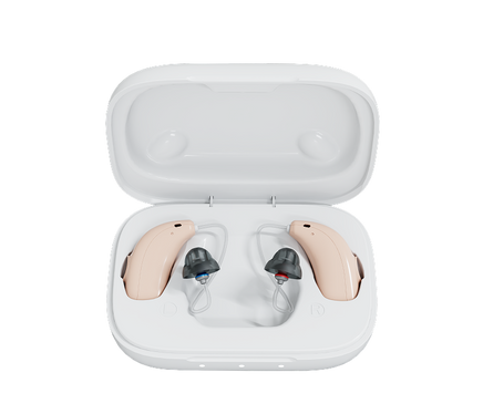 A pair of beige behind-the-ear hearing aids with dark gray ear tips, displayed inside an open white charging case on a solid white background.